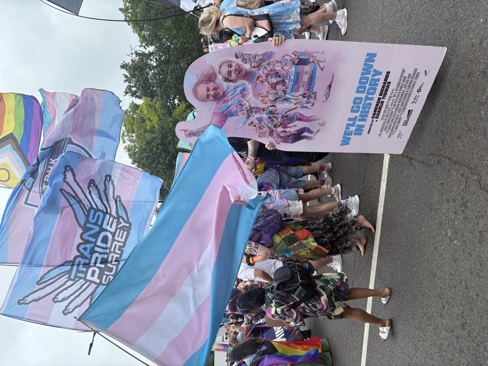 Trans flag and film poster carried at an outdoor march